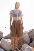 Earth Bermuda cotton shorts with relaxed tailored silhouette, front pleats and side pockets, styled with sheer organza shirt in warm coastal sunset light