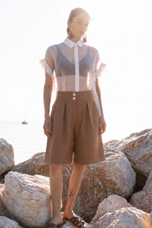 Earth Bermuda cotton shorts with relaxed tailored silhouette, front pleats and side pockets, styled with sheer organza shirt in warm coastal sunset light