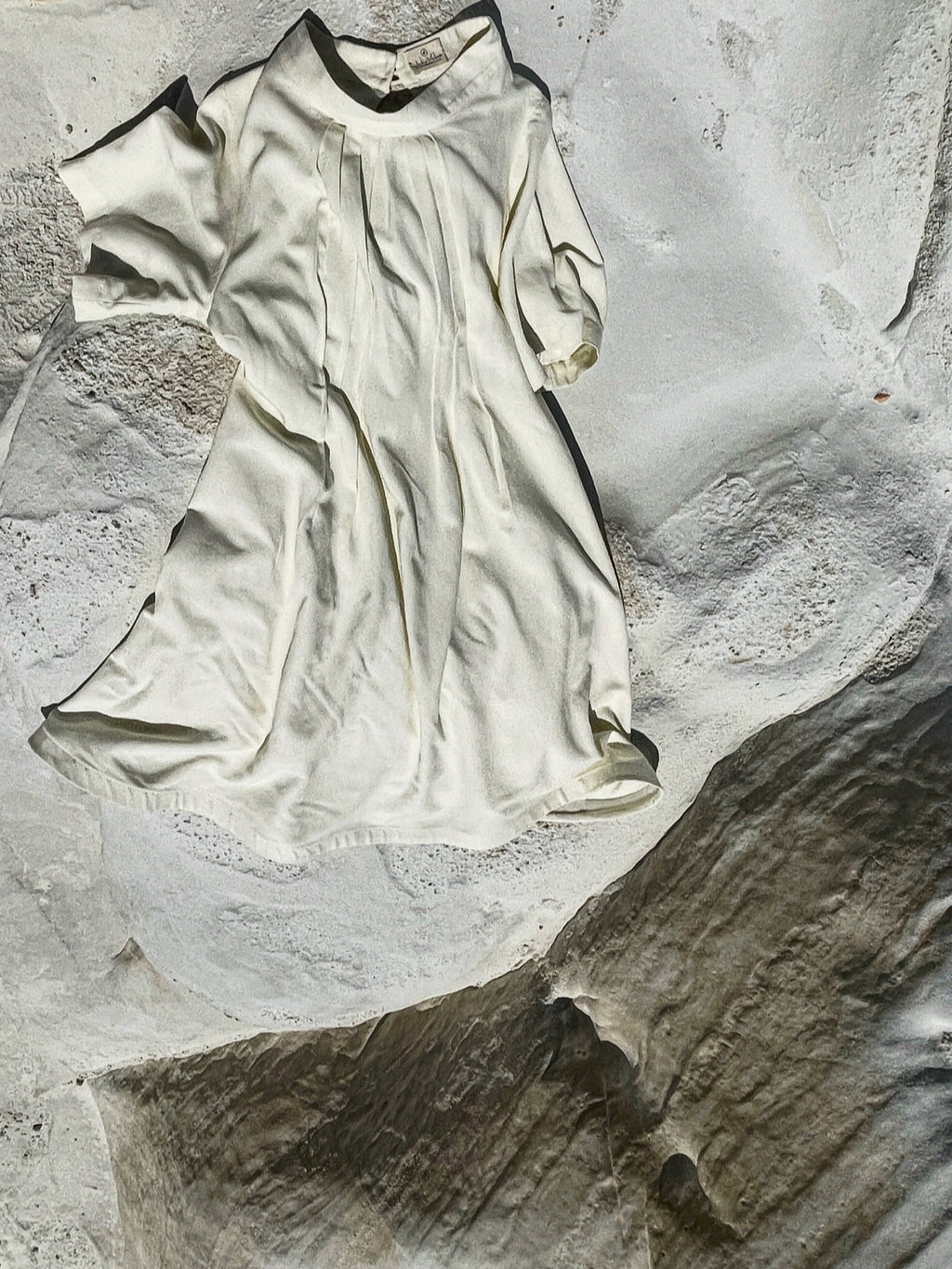 Cream linen-cotton dress with pleats laid on textured stone surface