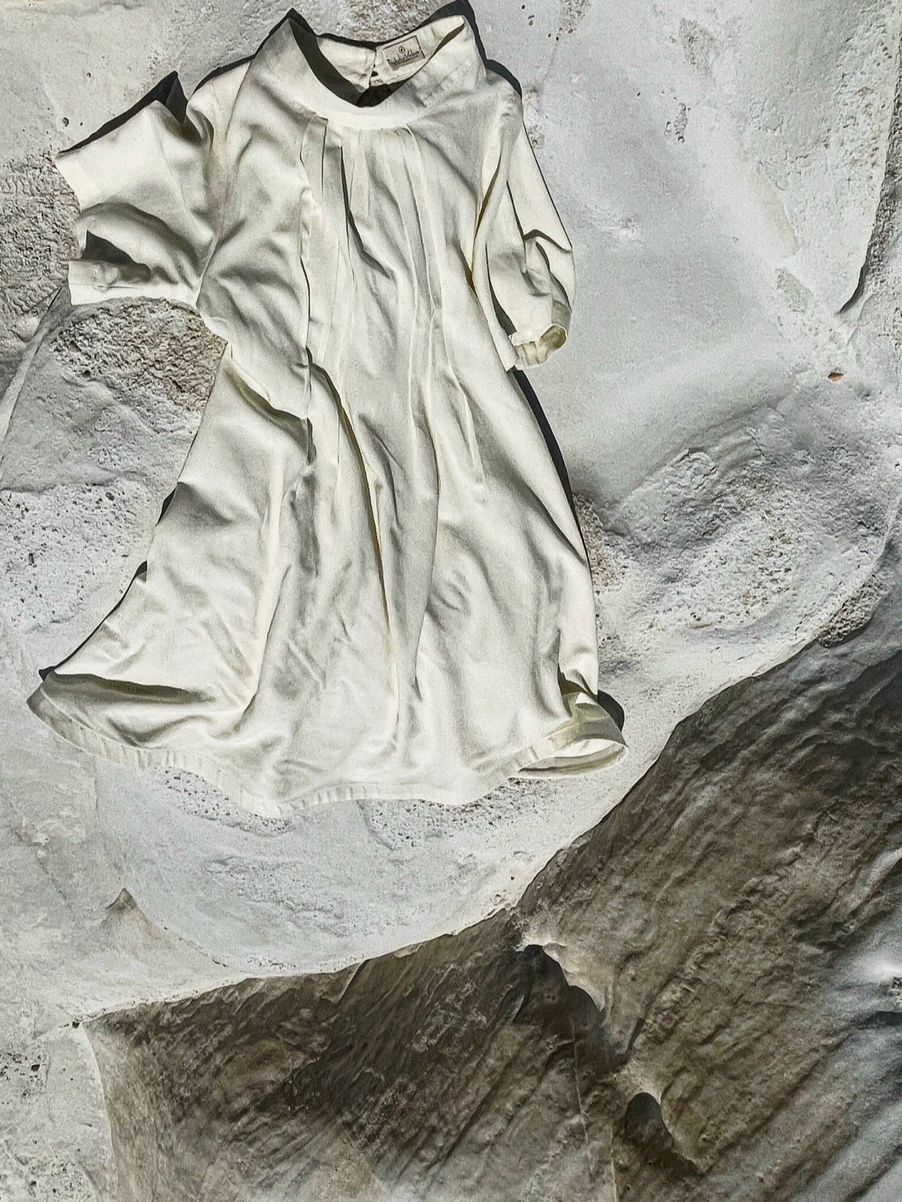 Cream linen-cotton dress with pleats laid on textured stone surface