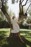 Cream linen-cotton dress with pleats worn under olive tree in natural light