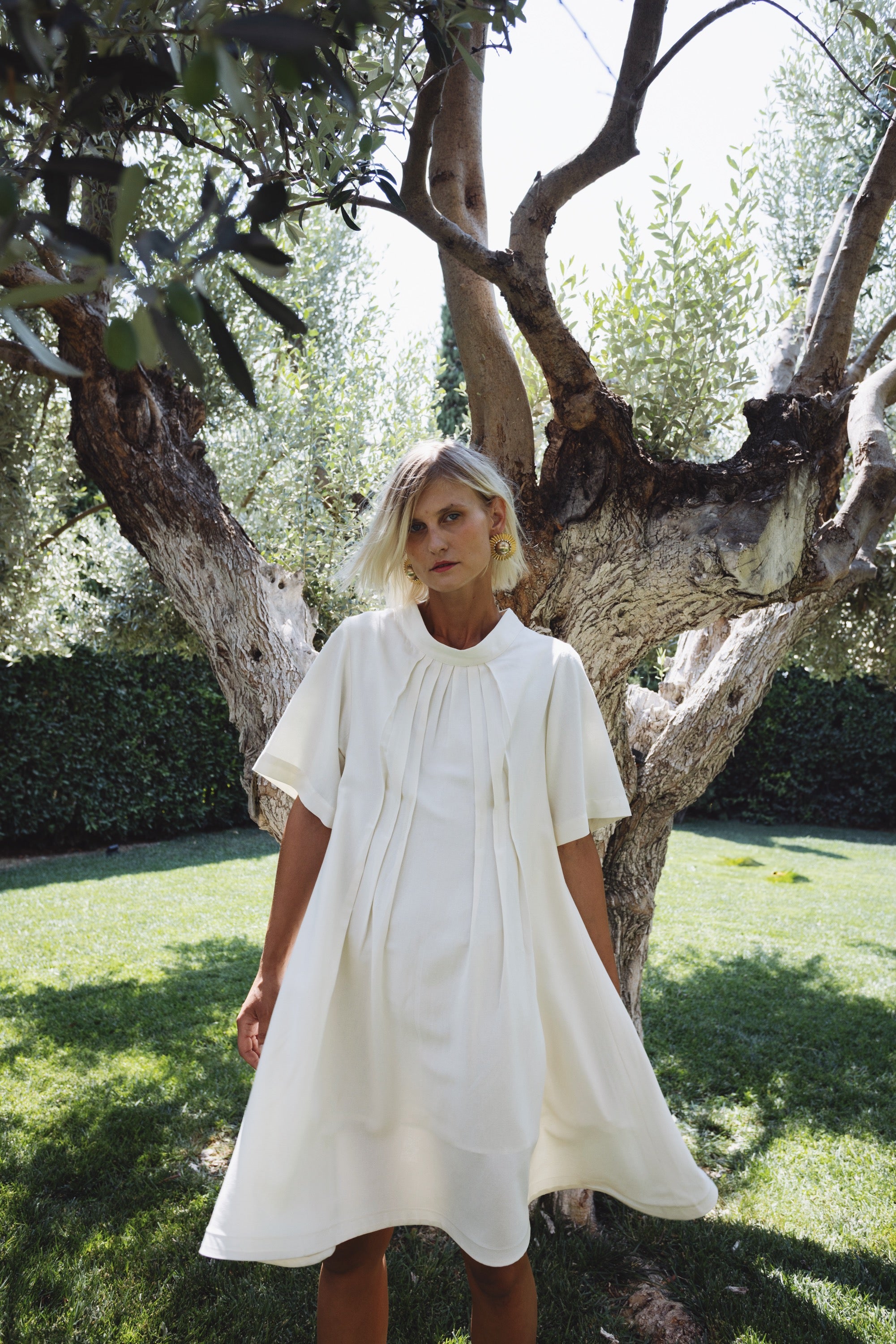 Cream linen-cotton dress with pleats in natural light under olive tree