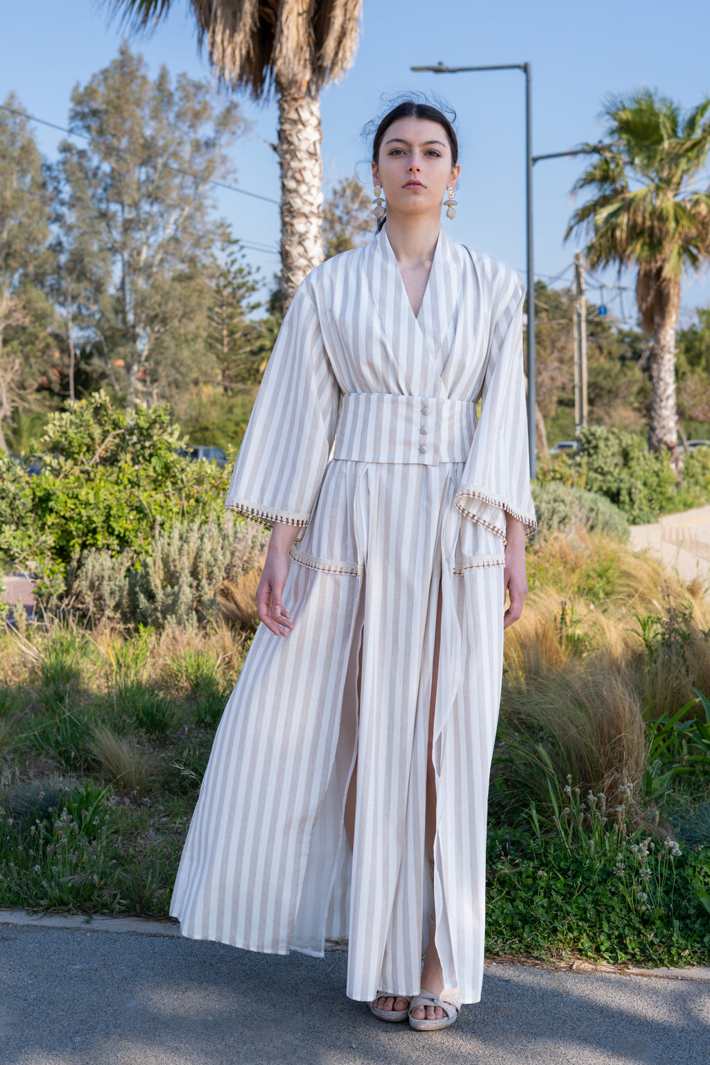 Striped cotton kimono dress with wide sleeves, belted waist with silver buttons and front slits, full body outdoor view