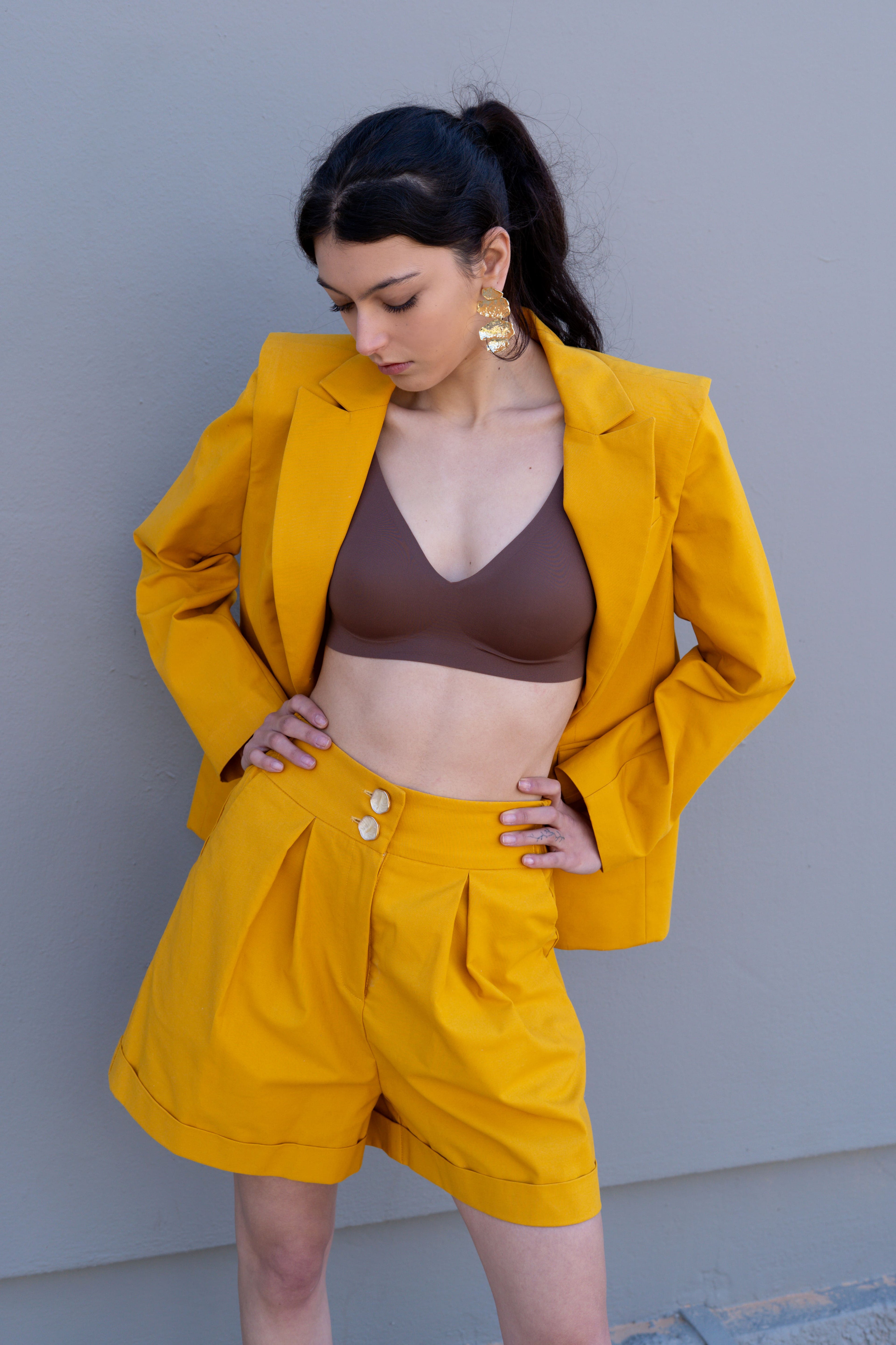Canary yellow high-waisted tailored bermuda shorts with front pleats and double button detail, styled with matching blazer, angled front view