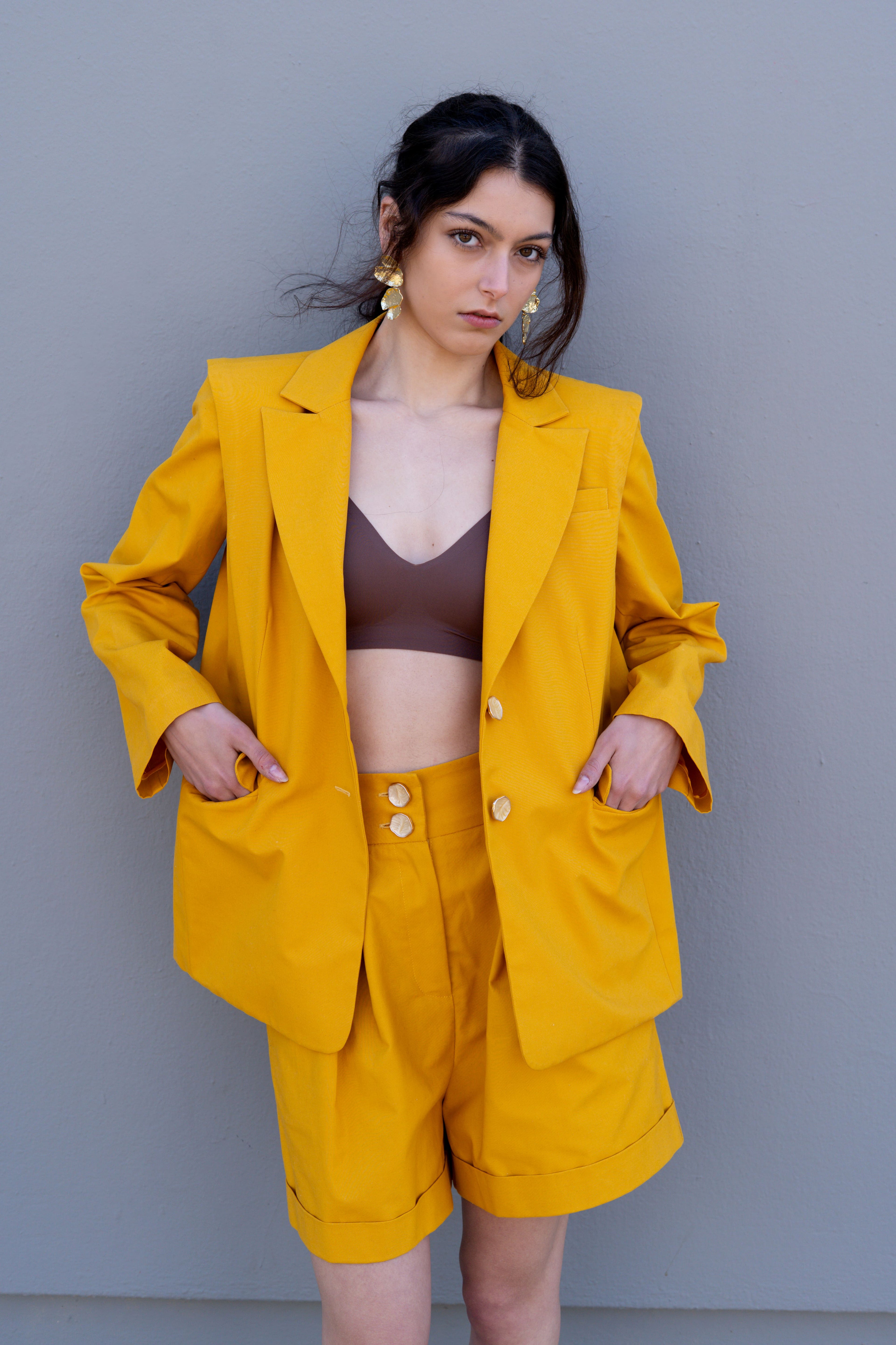 canary yellow tailored blazer with structured shoulders worn open hands in pockets styled with matching high waisted bermuda shorts