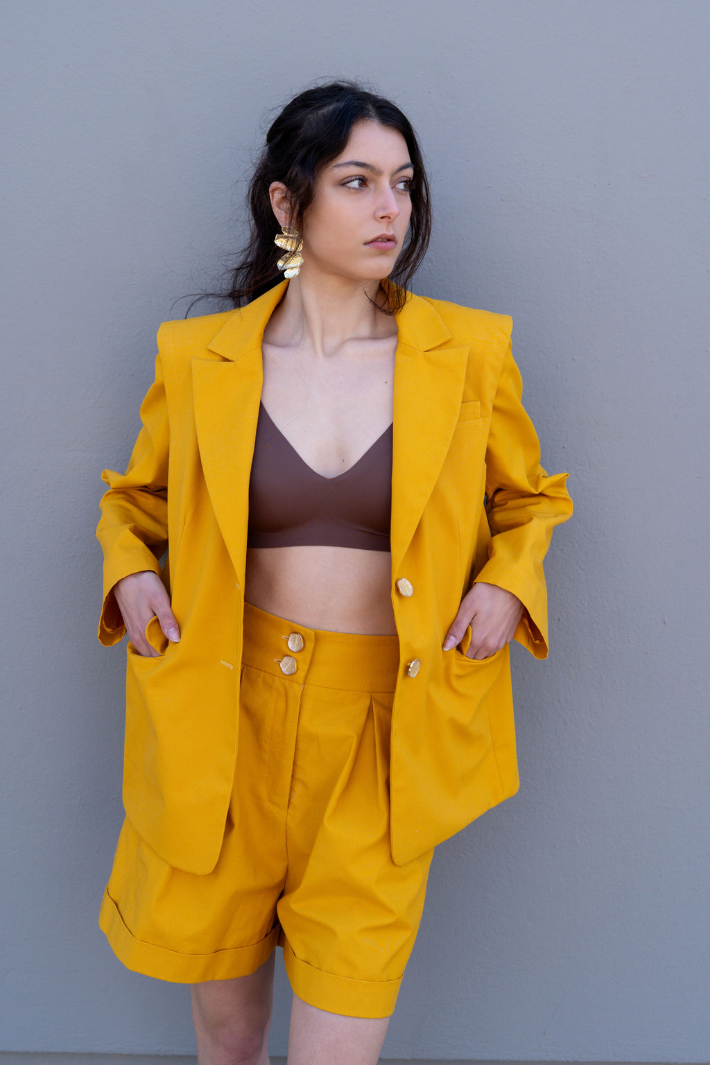 Canary yellow high-waisted tailored bermuda shorts with pleats and double button closure, styled with matching blazer, front three-quarter view