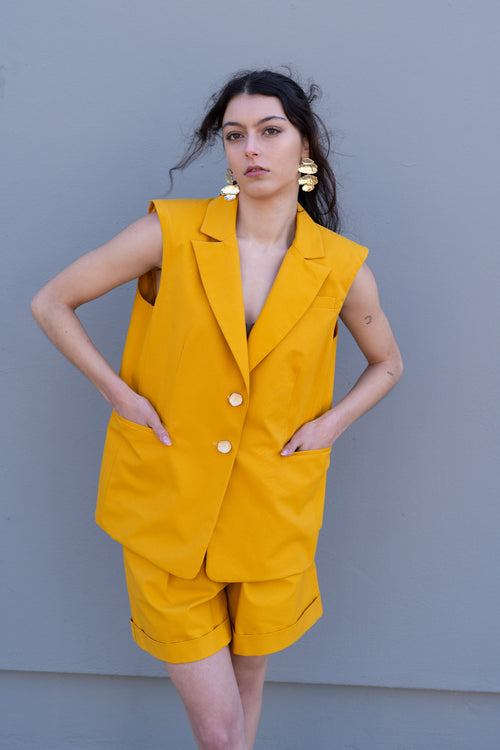 Canary yellow tailored vest with structured shoulders and front pockets, worn as a summer set with matching bermuda shorts
