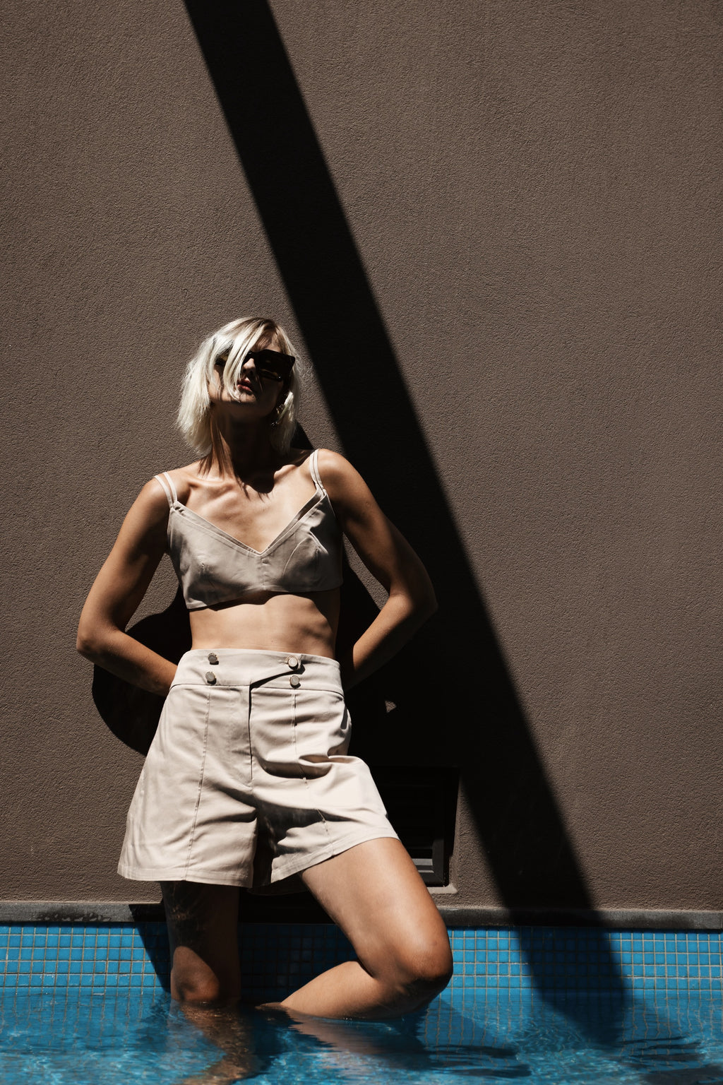 Beige high-waisted tailored bermuda with front button detail styled with Halo bralette in the pool – Julia Valas