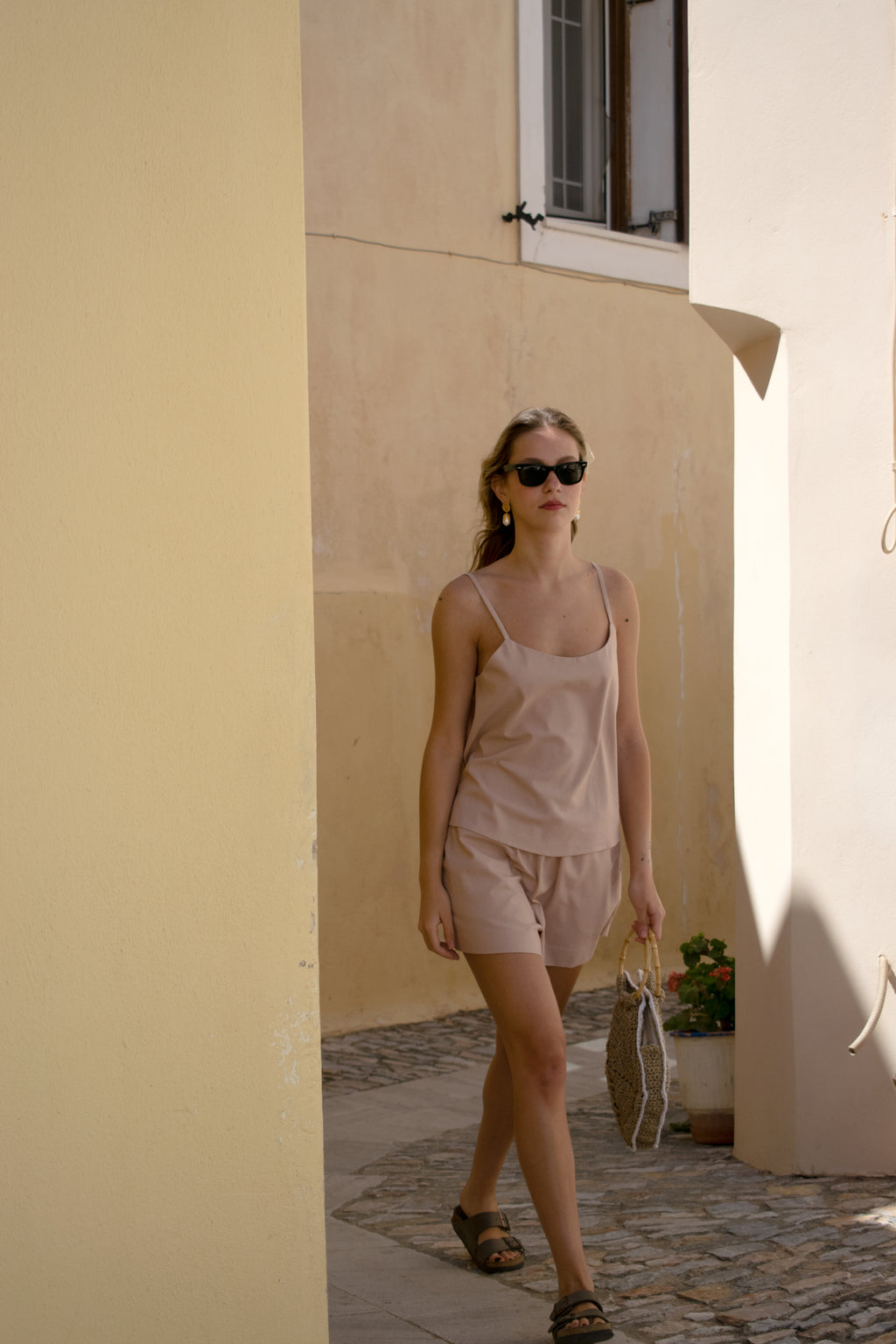 Julia Valas Sleep to Seaside Set in Rose Sand featuring a linen camisole top and relaxed shorts, walking in the alley front view.