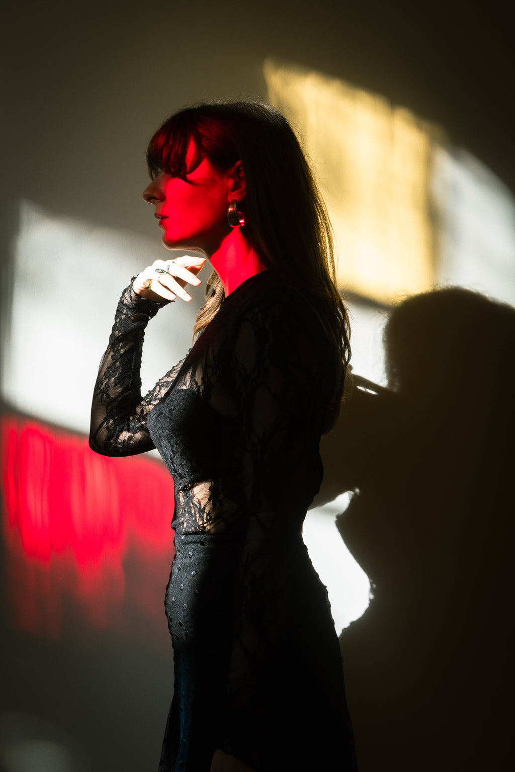 Black lace long-sleeve bodysuit with built-in cups, side profile of model with dramatic red and warm light shadows, sculpted silhouette, Julia Valas