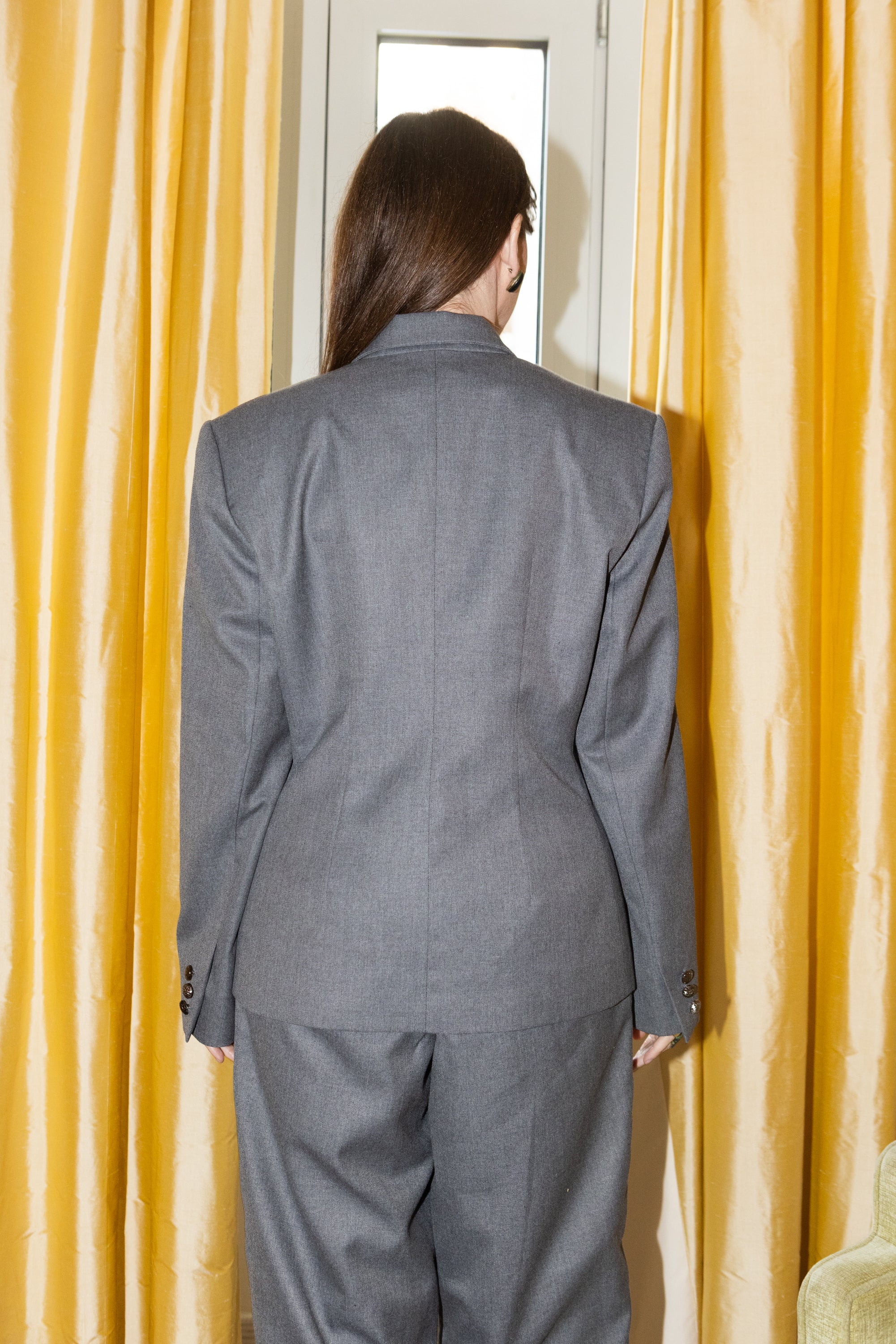Grey oversized tailored blazer set back view, structured shoulders and clean silhouette, gold curtain backdrop, editorial fashion styling