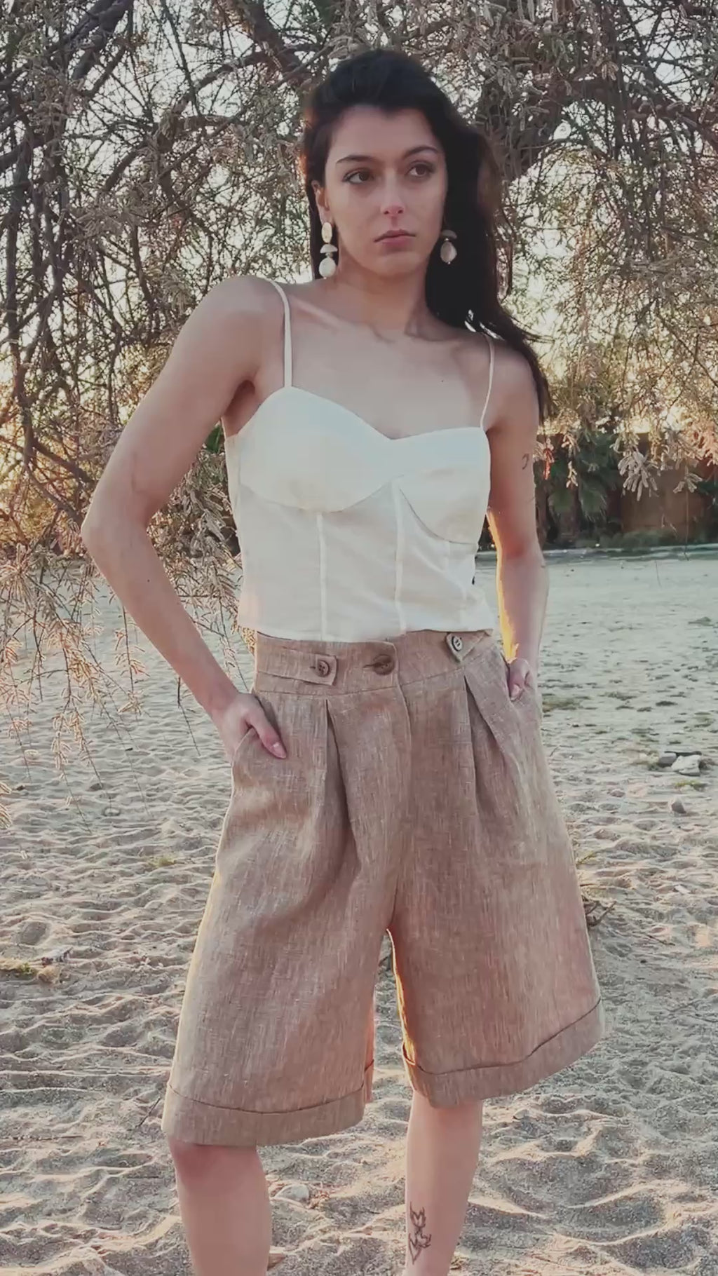 Sweetheart cotton silk bustier top with structured cups and thin straps paired with Smart Volume bermuda pants, high-waisted pleated tailored silhouette in lightweight linen fabric. Video at the beach during sunset.