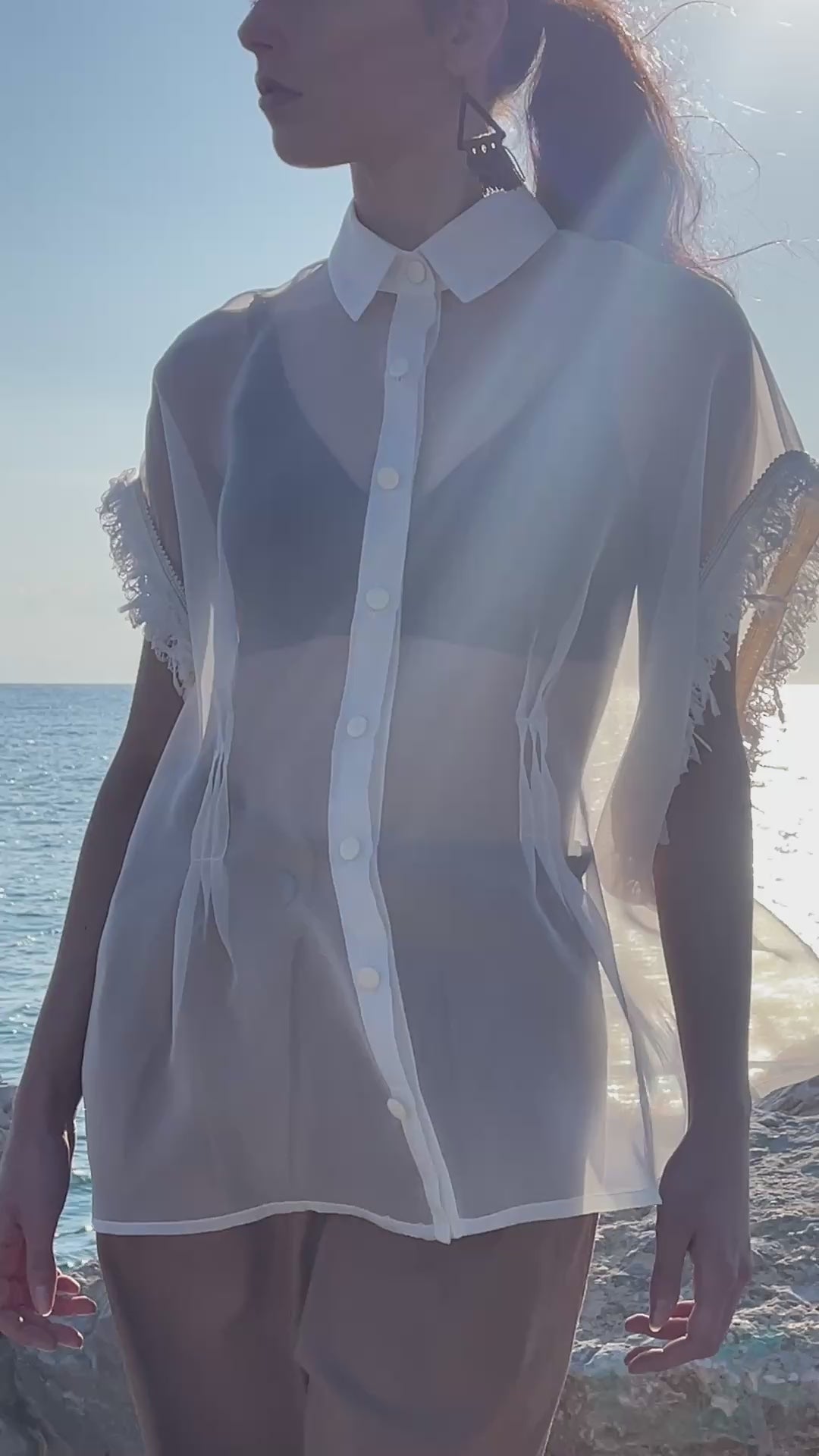 Sheer silk organza shirt with structured collar, matte flat buttons and fringed trim sleeves, styled over neutral bralette and relaxed high waisted tailored trousers in warm coastal sunset light