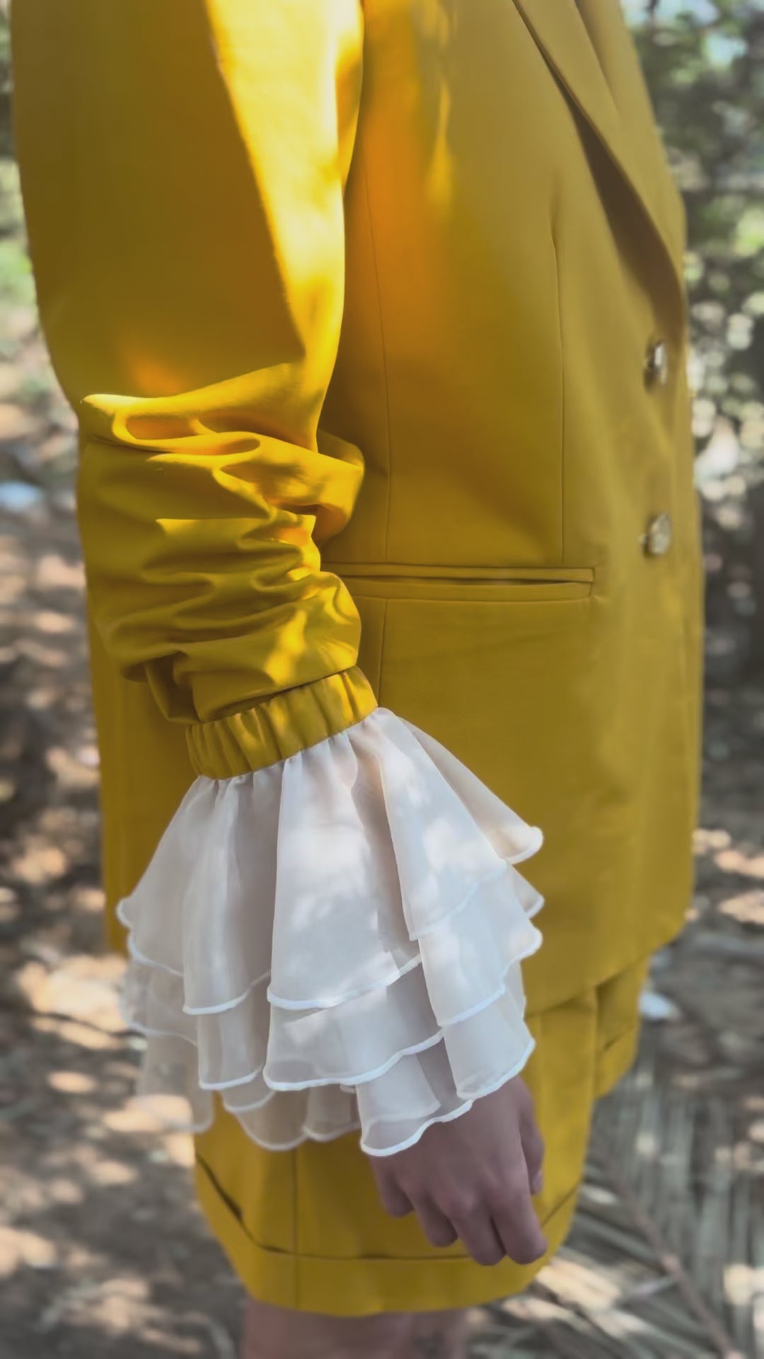 canary yellow tailored blazer video with detachable sleeves detachable ruffled cuffs open back teardrop cutout and floral lace back view model standing in nature