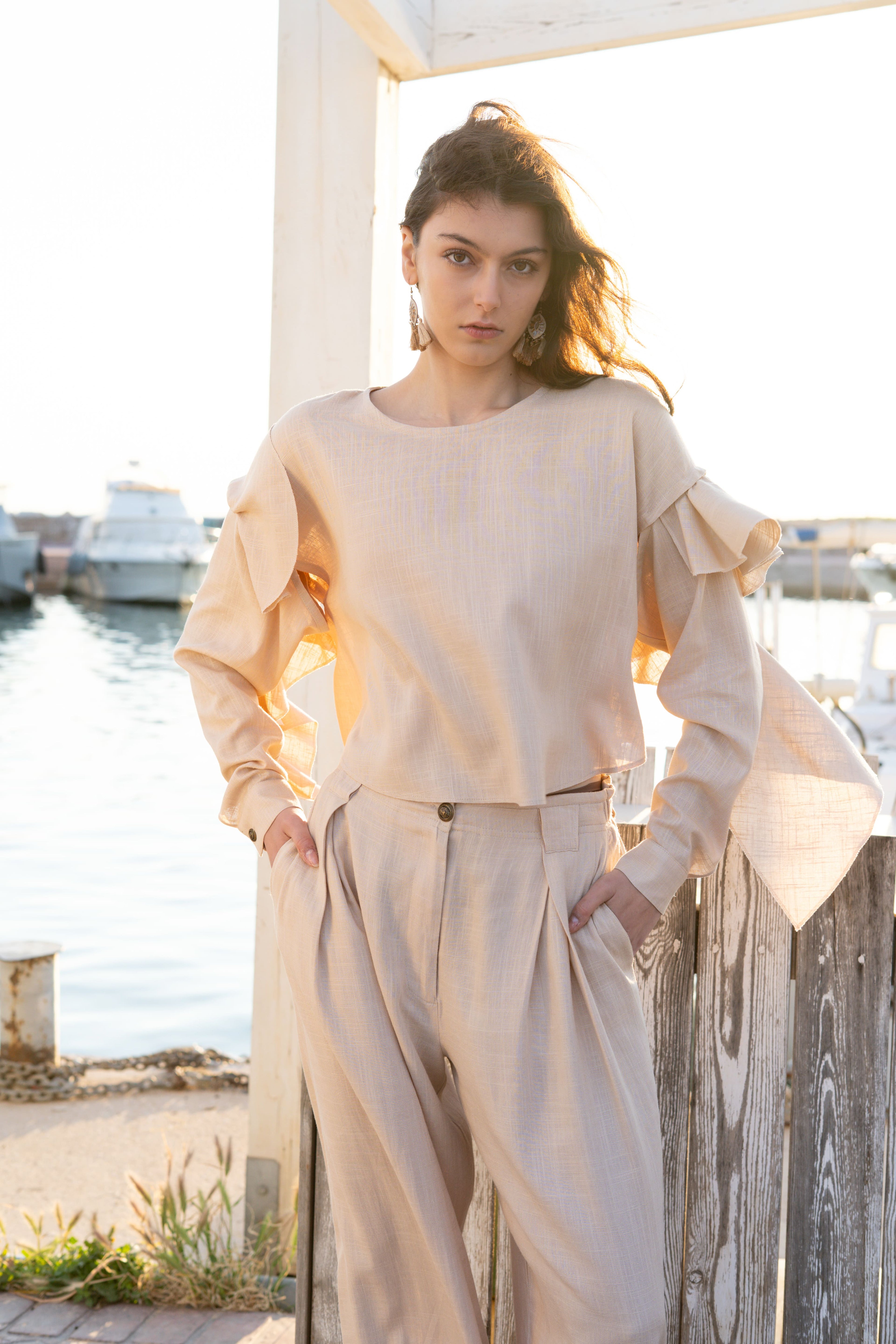 Ruffled linen viscose top with detachable sleeves paired with relaxed pleated tapered pants, elegant soft neutral womenswear in coastal sunset light by Julia Valas