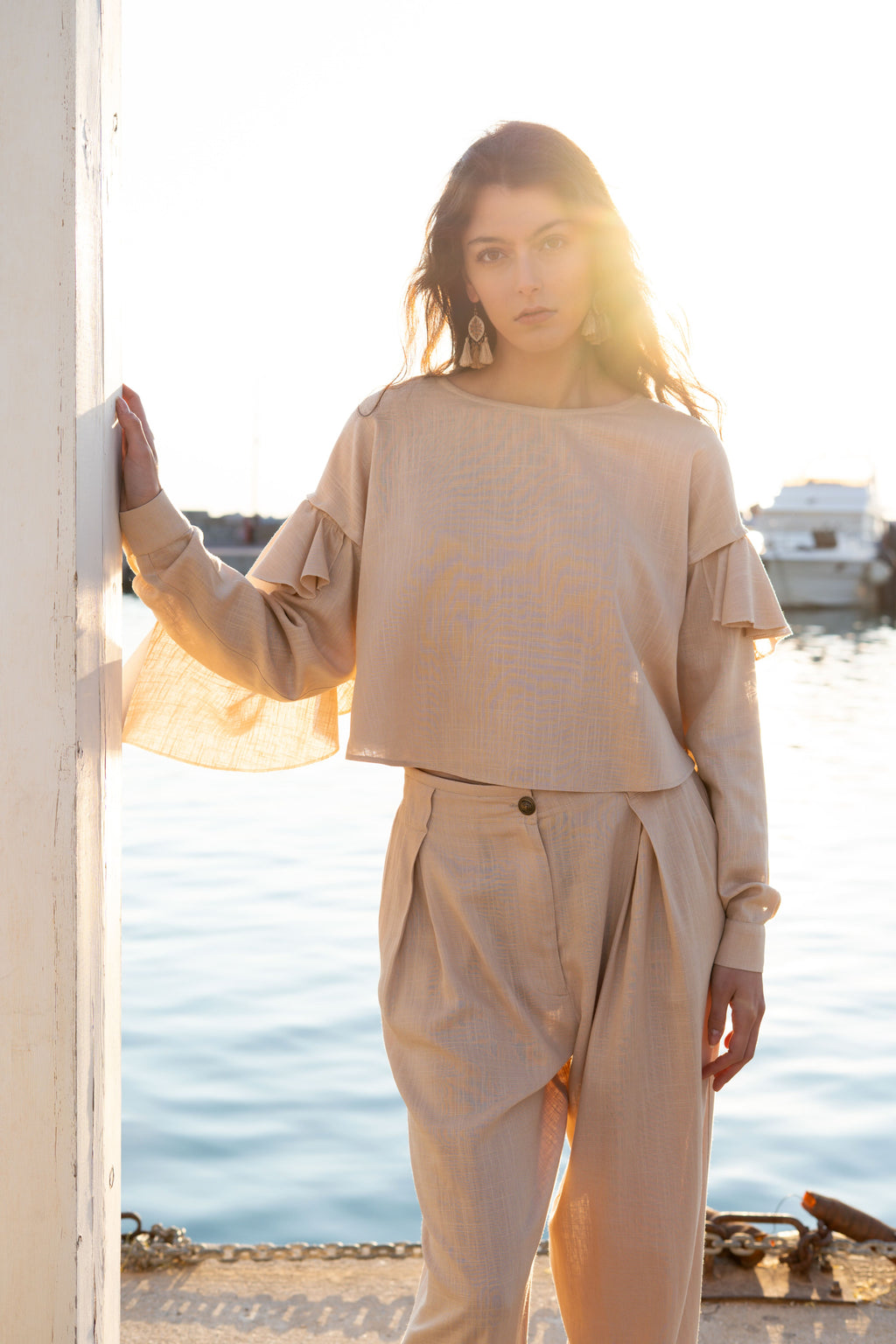 Ruffled linen viscose top with detachable sleeves and soft ruffle detail, relaxed cropped silhouette styled in warm sunset light