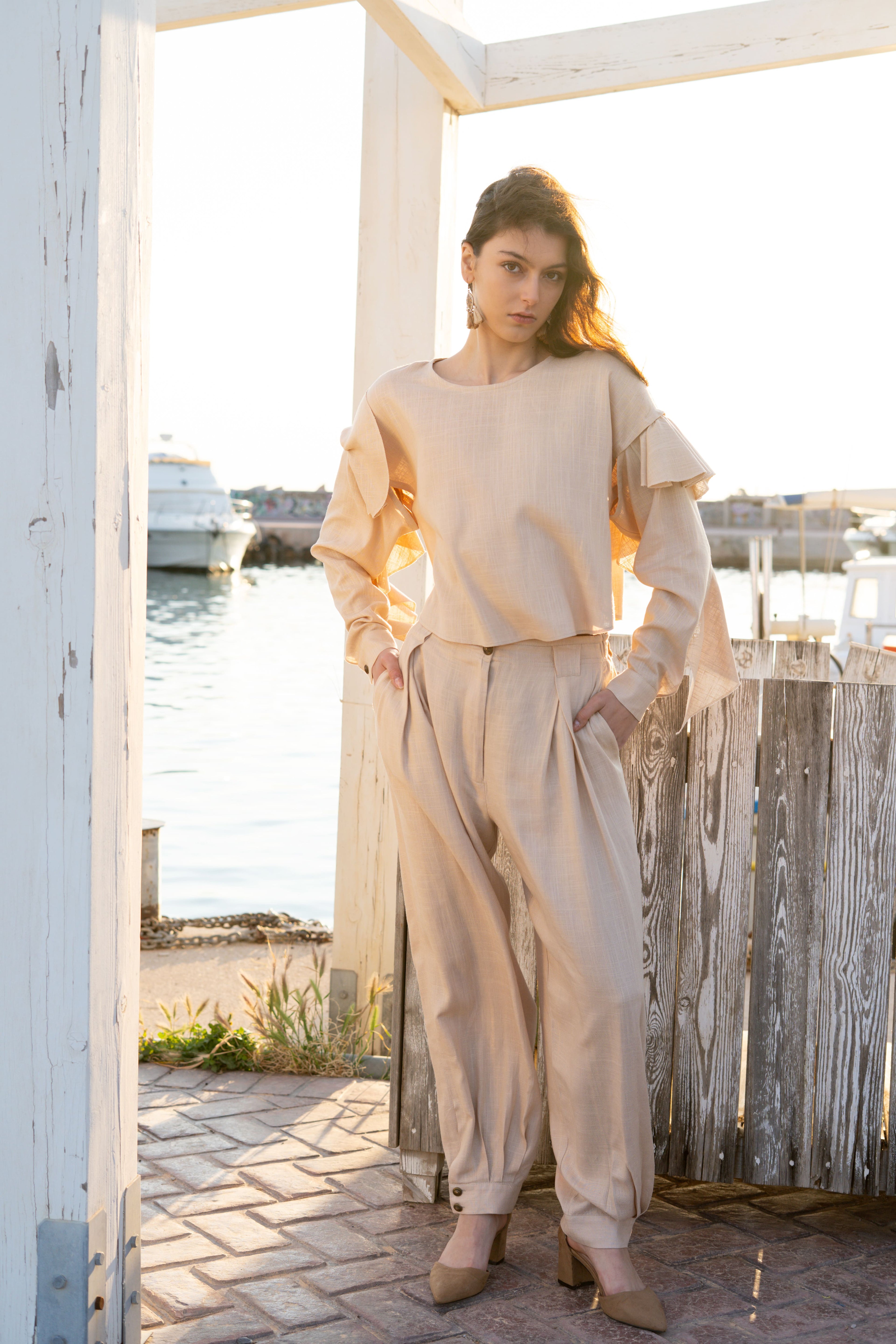 Ruffled linen viscose top with detachable sleeves paired with relaxed pleated tapered pants, soft layered ruffles and elegant summer silhouette in natural sunset light by Julia Valas