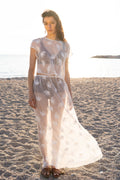 Full-length view of the Thalassa Sheer Set with embroidered transparent top and flowing sheer maxi skirt, lightweight resort silhouette on a sandy beach at sunset by Julia Valas