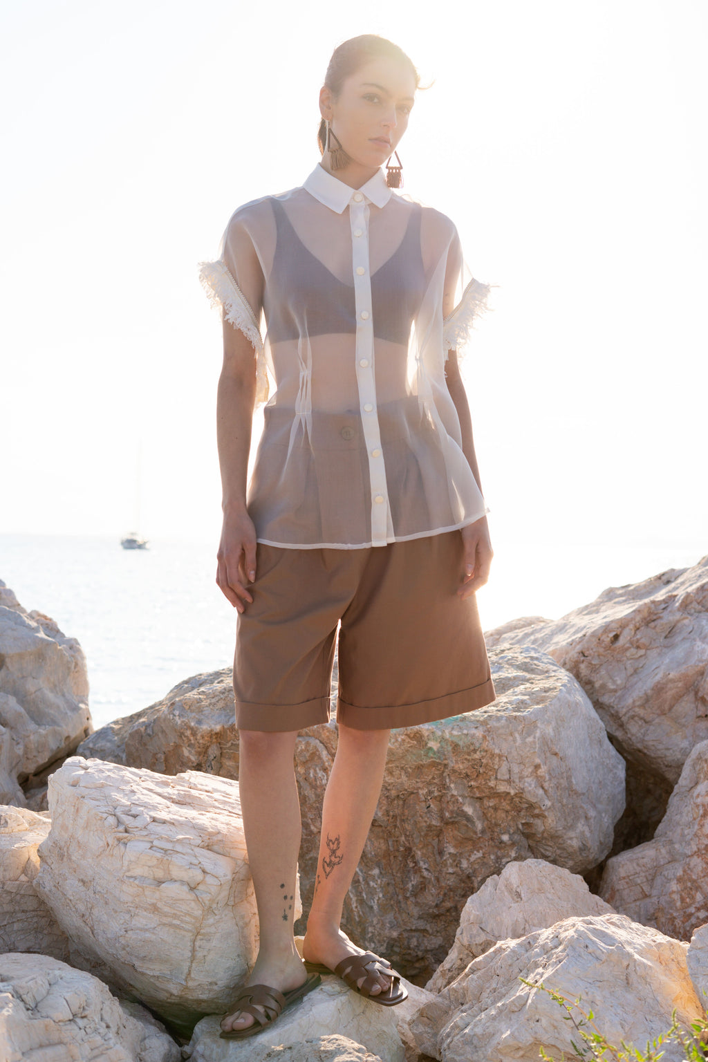 Sheer silk organza shirt with structured collar, matte flat buttons and fringed trim sleeves, styled with relaxed bermuda shorts in warm seaside sunset light